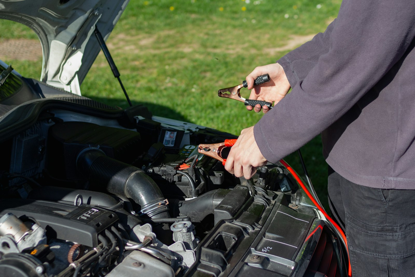 Mecánico conectando cables de partida a la batería de un auto en la calle